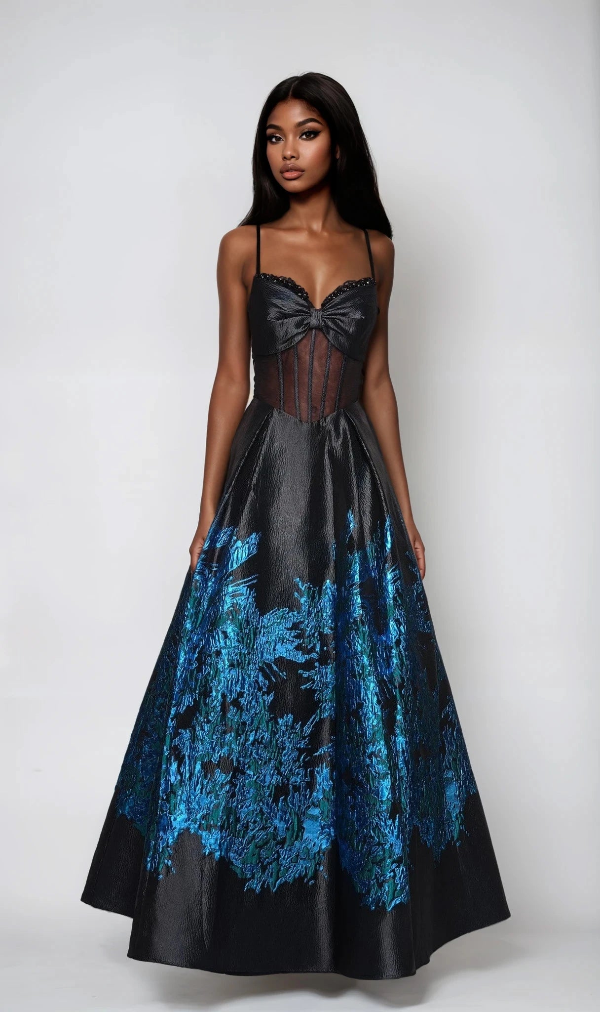 A woman stands against a plain background wearing the Dave and Johnny 12702 long prom dress, featuring a black sheer corset bodice and a voluminous, iridescent floral skirt.